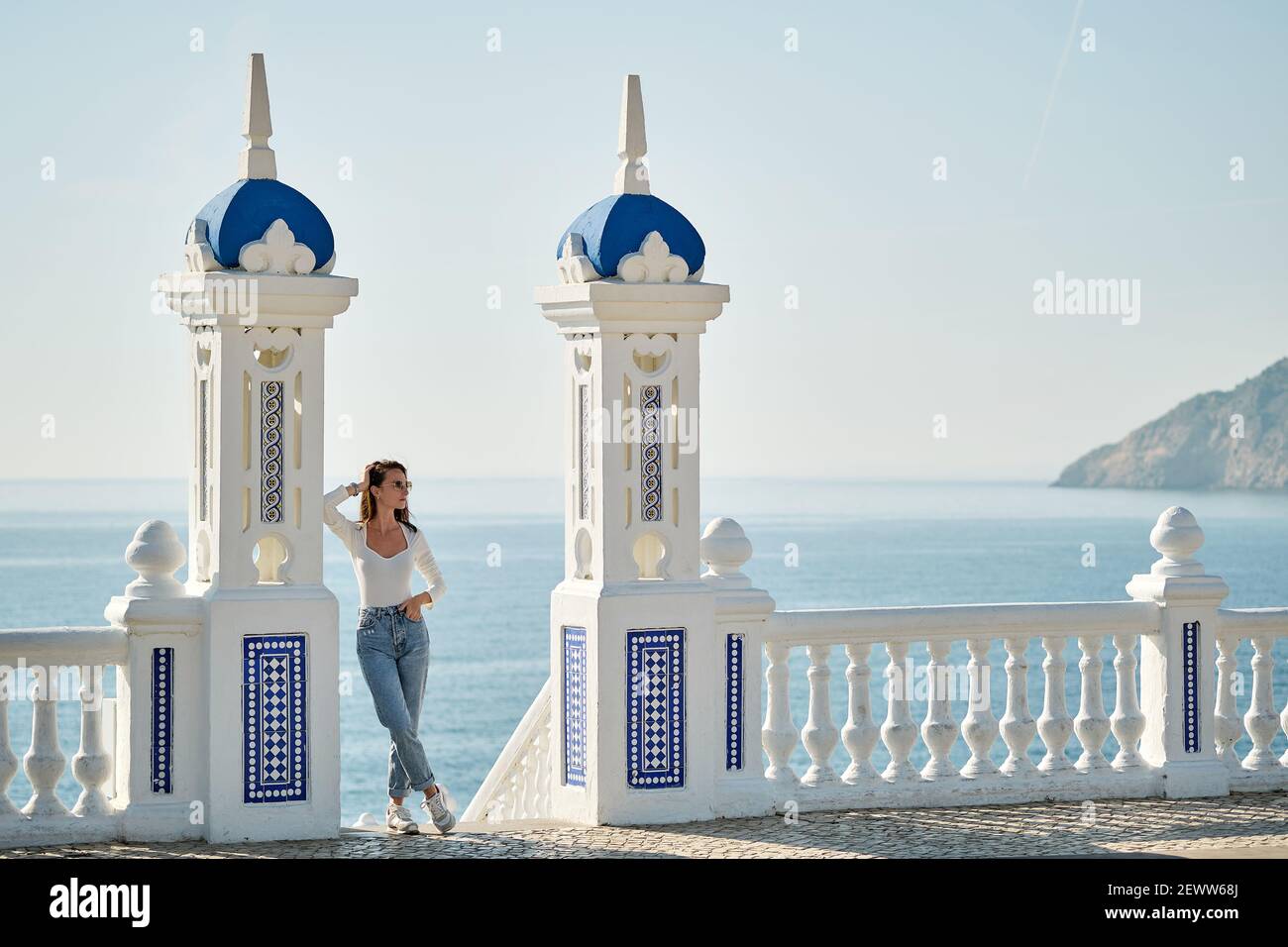 Giovane bella donna posa in turistico Balcon del Mediterraneo. Balaustra dipinta di bianco con vista sul mare blu durante la soleggiata giornata invernale, famosa località di Beni Foto Stock