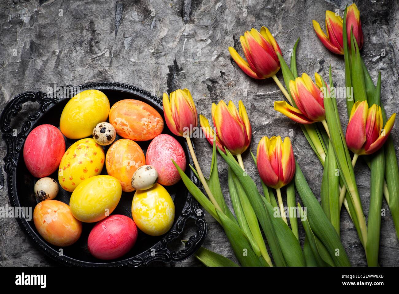 Tulipani colorati rossi e gialli con uova di Pasqua dipinte a mano su un tavolo in legno con spazio per la copia Foto Stock