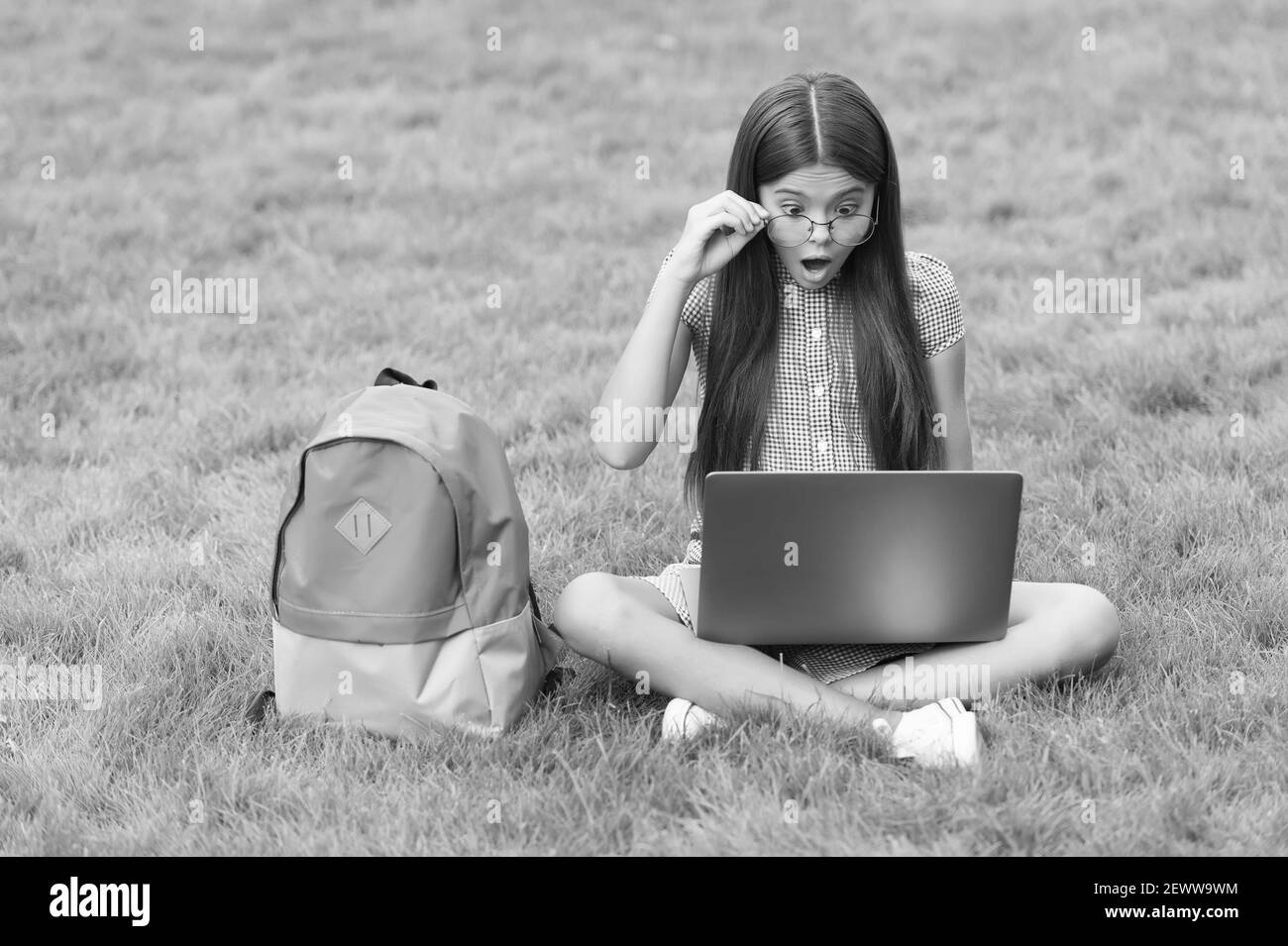 bambino sorpreso in occhiali guardando lo schermo mentre si gioca al computer su un computer portatile nel parco, intrattenimento infantile. Foto Stock