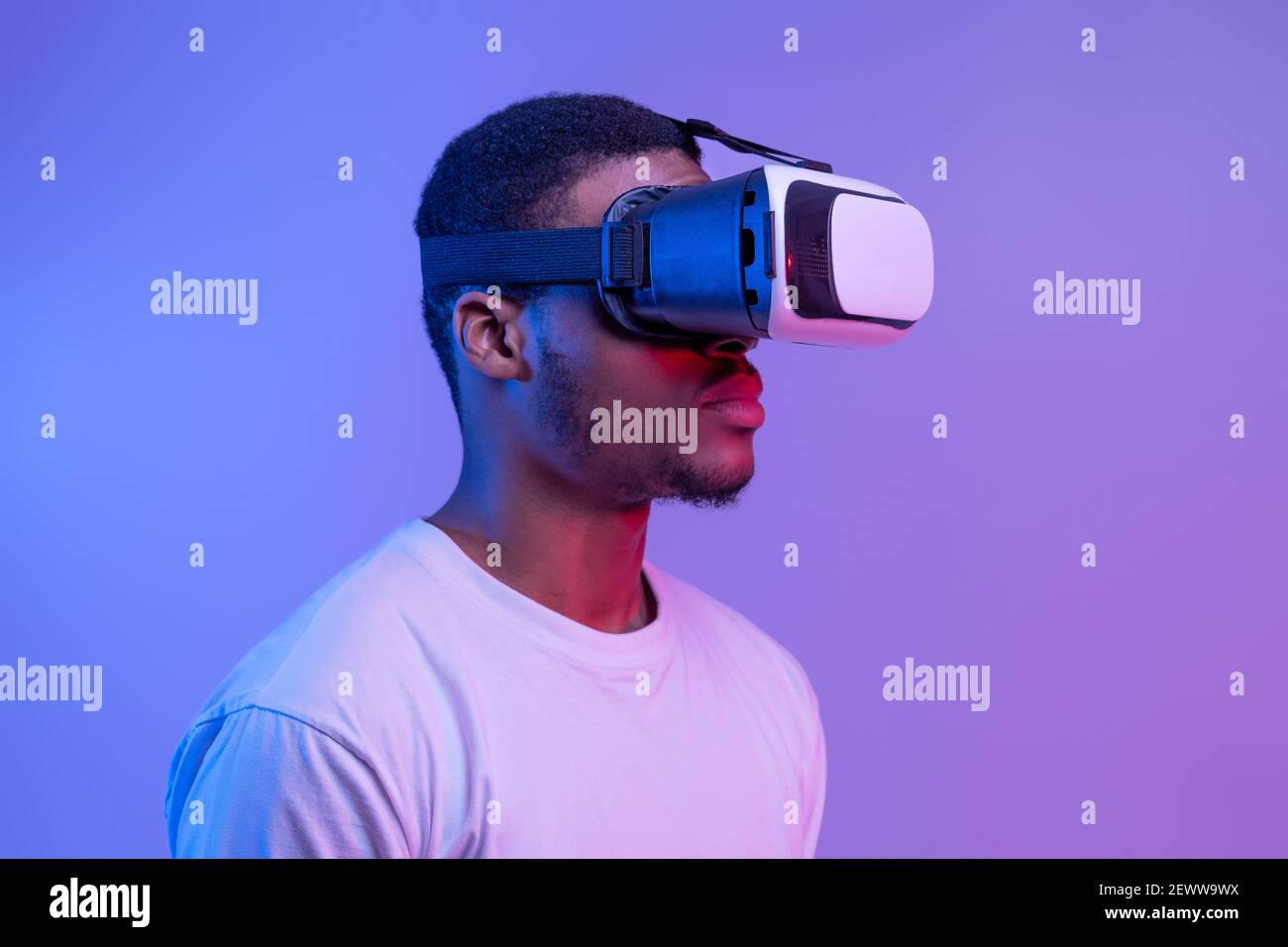 Black Man in VR Headset in piedi in Neon Light Over Sfondo viola Foto Stock