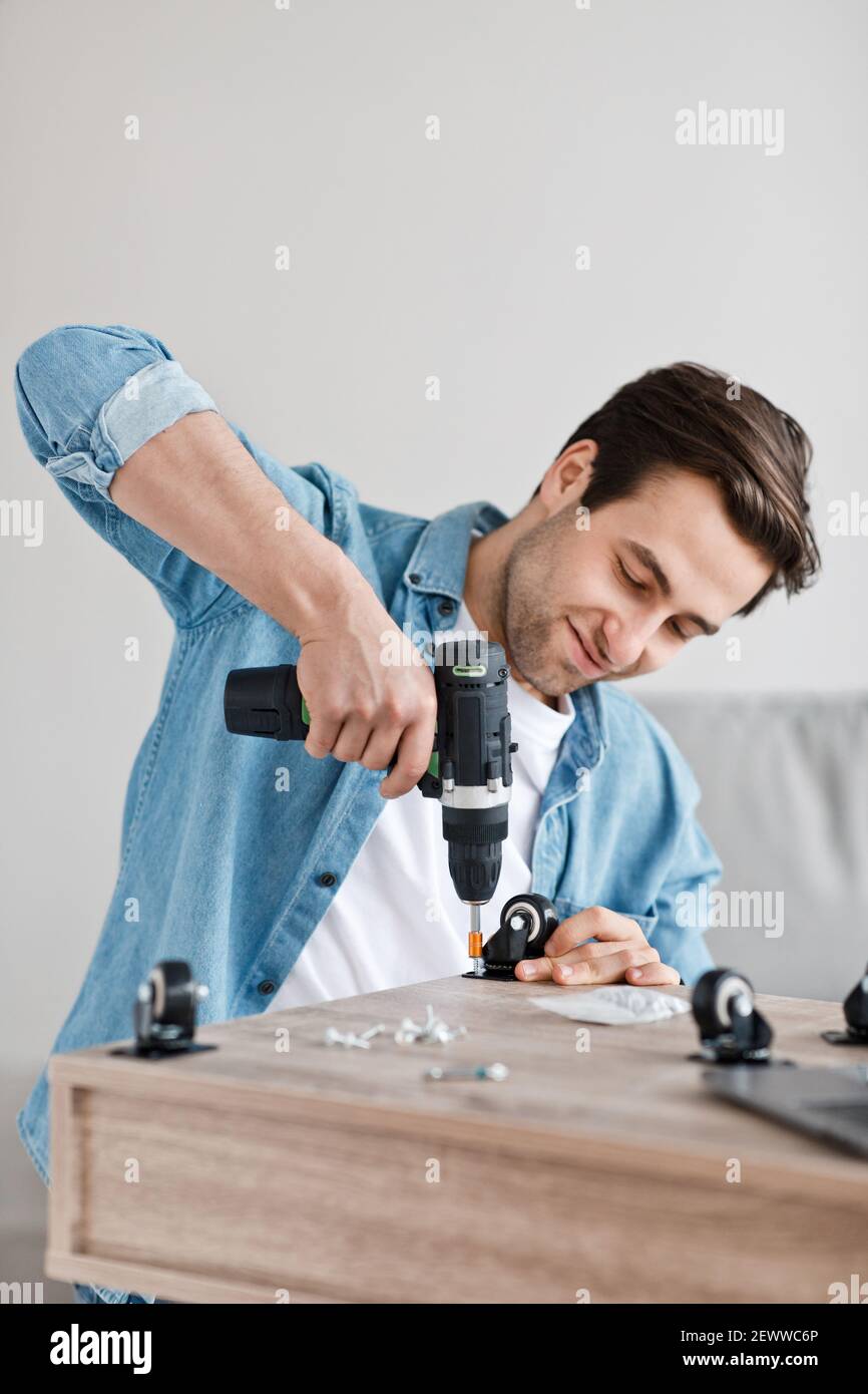 Il trapano elettrico funziona nelle mani di handyman, assembla e ripara i mobili a casa Foto Stock