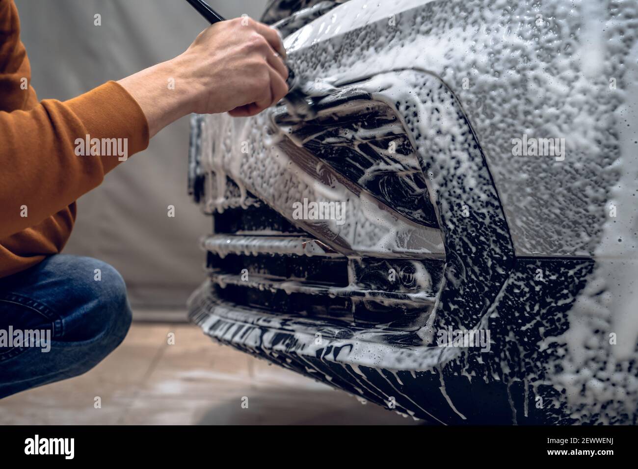 Dettagli per autolavaggio. Il lavoratore pulisce il paraurti con la schiuma e la spazzola per shampoo automatico, la pulizia dettagliata del veicolo, primo piano. Foto Stock