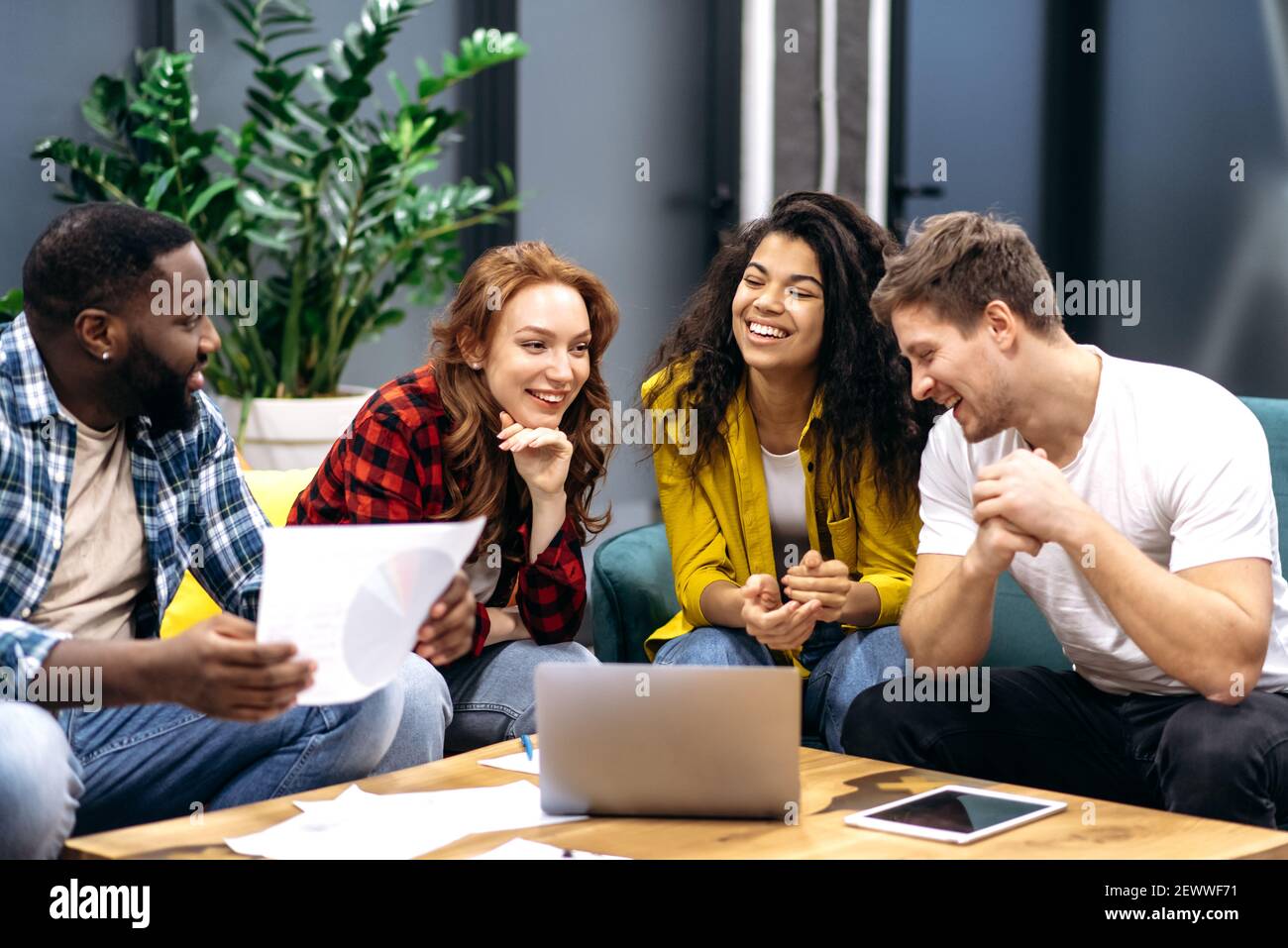 Amichevole team di business multirazziale, seduto in ufficio, parlando di processo di lavoro, sorridente, comunicare tra loro, discutere di nuove startup, studiare grafici finanziari Foto Stock