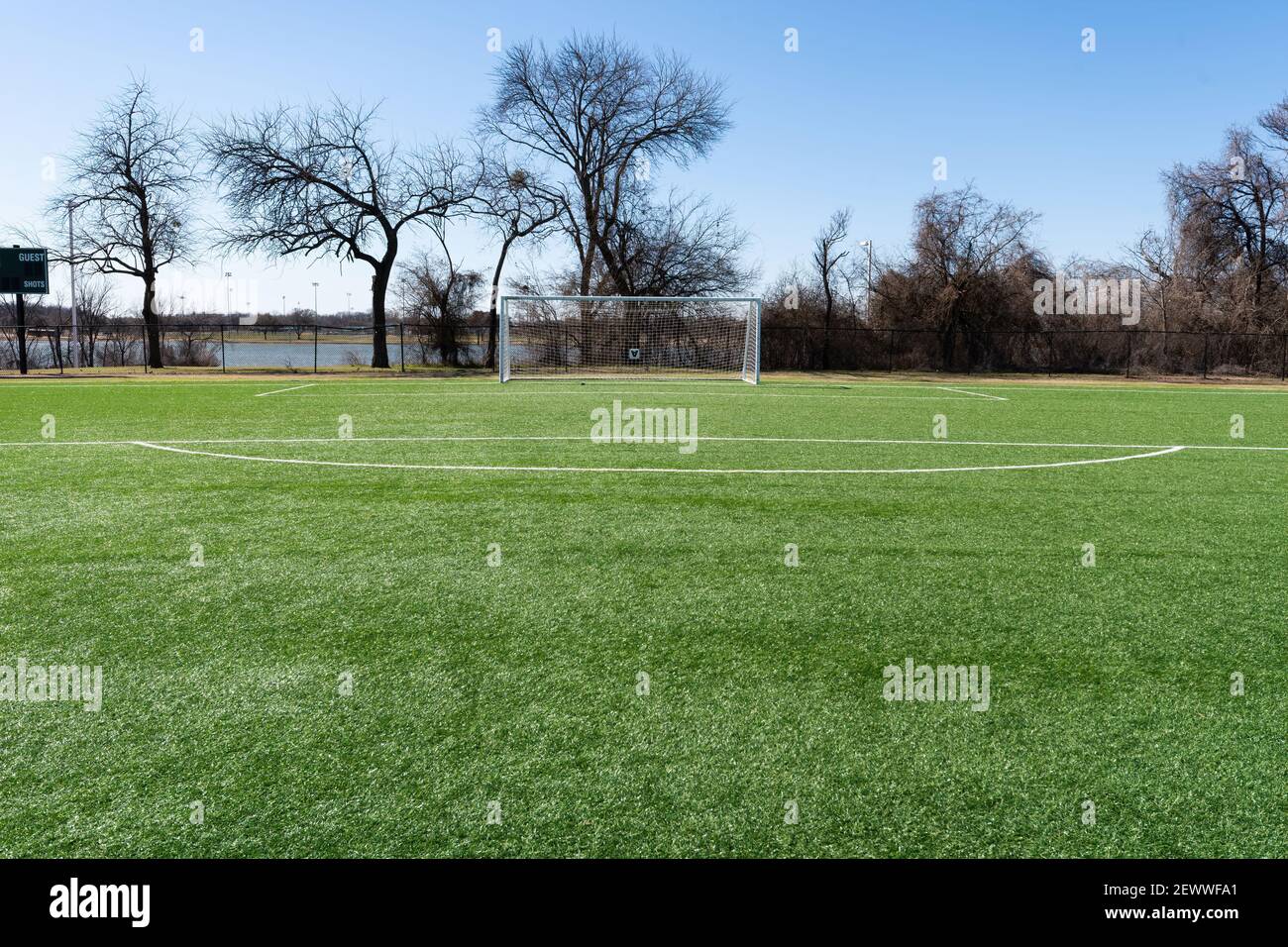 Calcio su un campo con erba artificiale in un parco cittadino con alberi e un lago sullo sfondo. Foto Stock