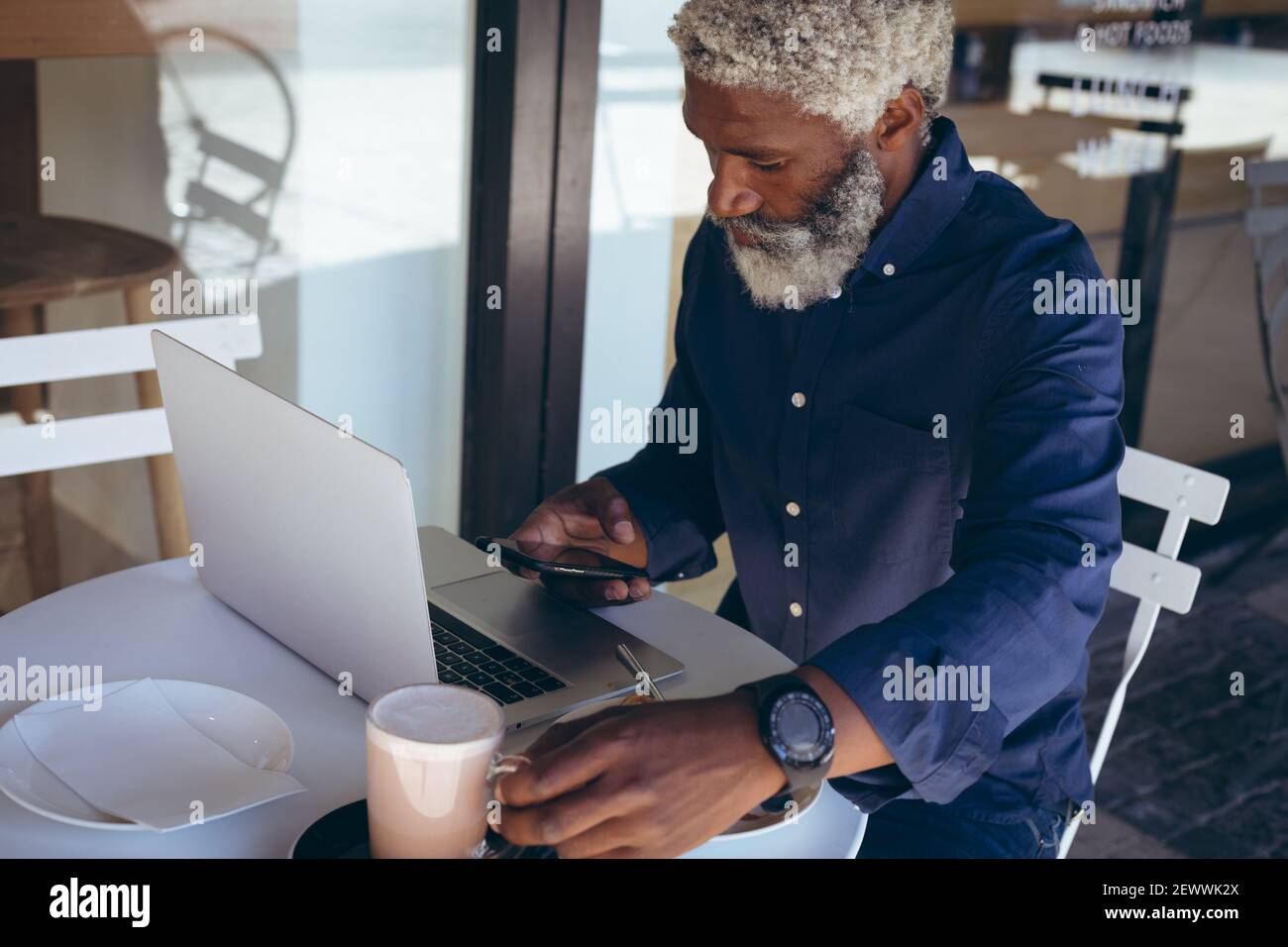 Uomo anziano afroamericano seduto al tavolo all'esterno del caffè computer portatile e smartphone Foto Stock