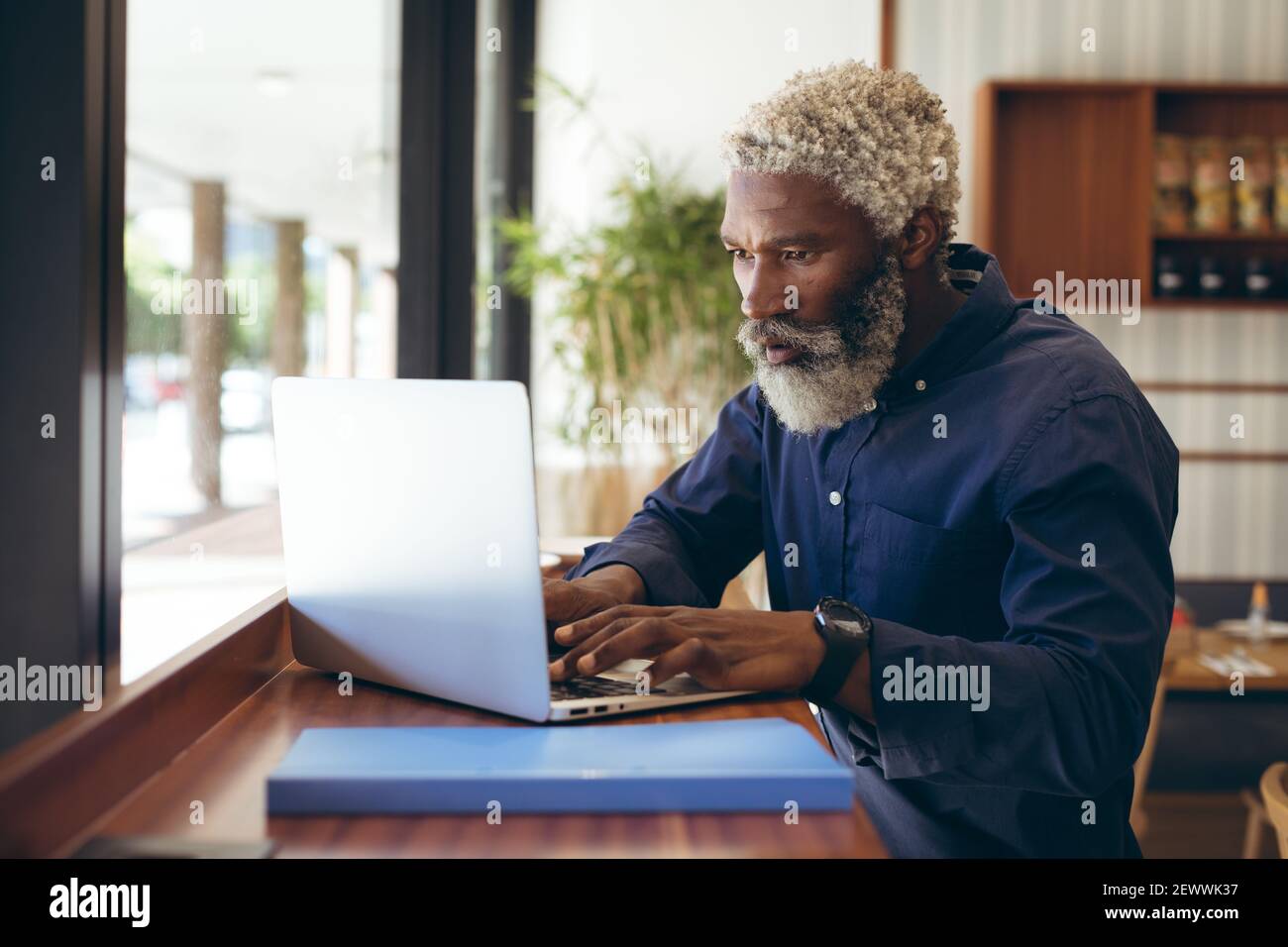 Uomo anziano afroamericano seduto al tavolo in un bar che lavora utilizzando un computer portatile Foto Stock