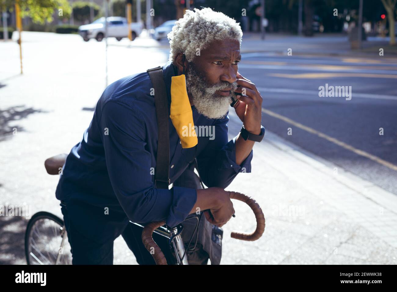 Uomo anziano afro-americano che indossa la maschera che pende sulla bicicletta in strada che parla con lo smartphone Foto Stock