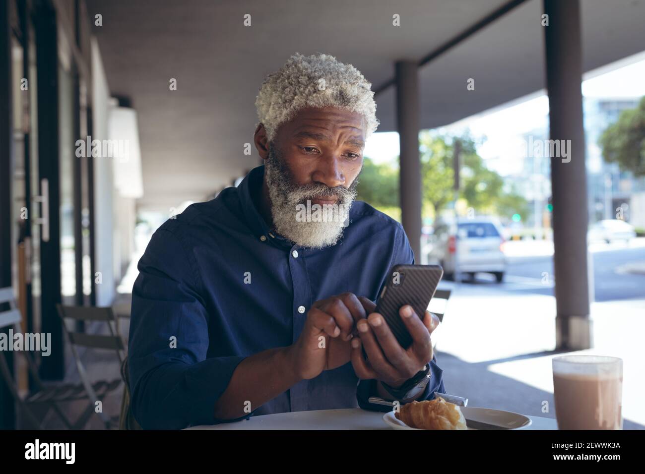 Uomo anziano afroamericano seduto al tavolo fuori del cafe con caffè con smartphone Foto Stock