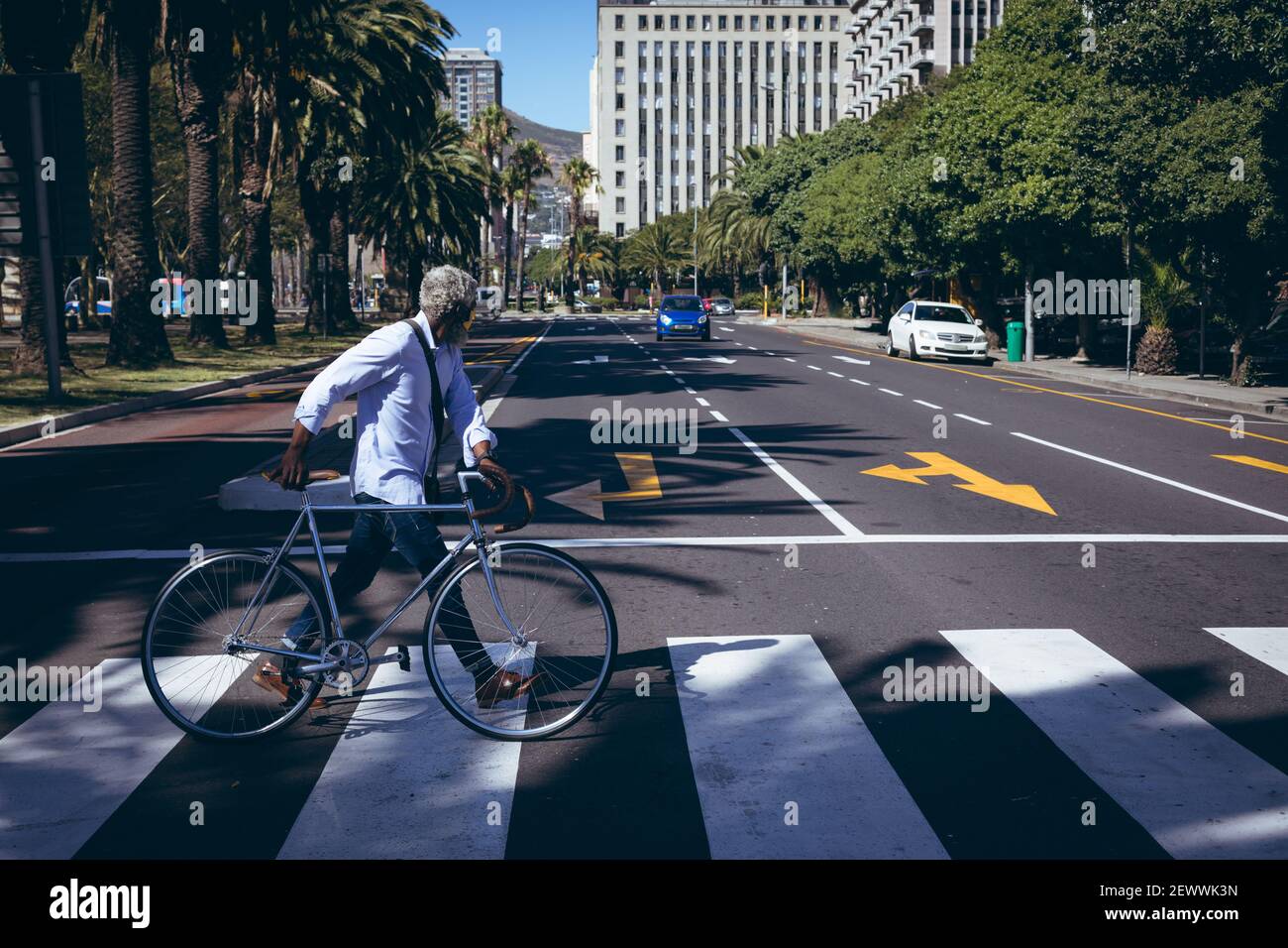 L'uomo anziano afro-americano che ruota in bicicletta attraverso la strada su un attraversamento pedonale Foto Stock