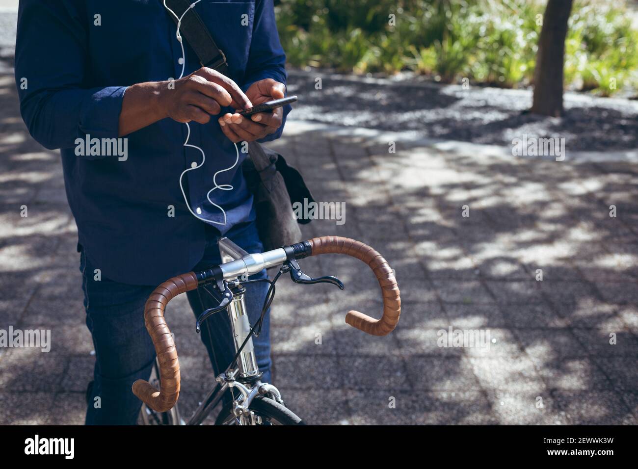 Sezione centrale dell'uomo anziano afroamericano che indossa gli auricolari seduti sopra bicicletta in strada utilizzando smart Foto Stock
