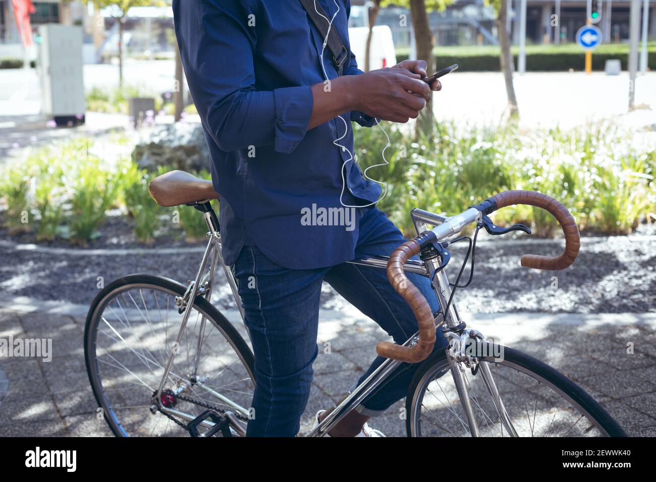 Sezione bassa dell'uomo anziano afroamericano che indossa gli auricolari seduti in bicicletta in strada utilizzando smar Foto Stock