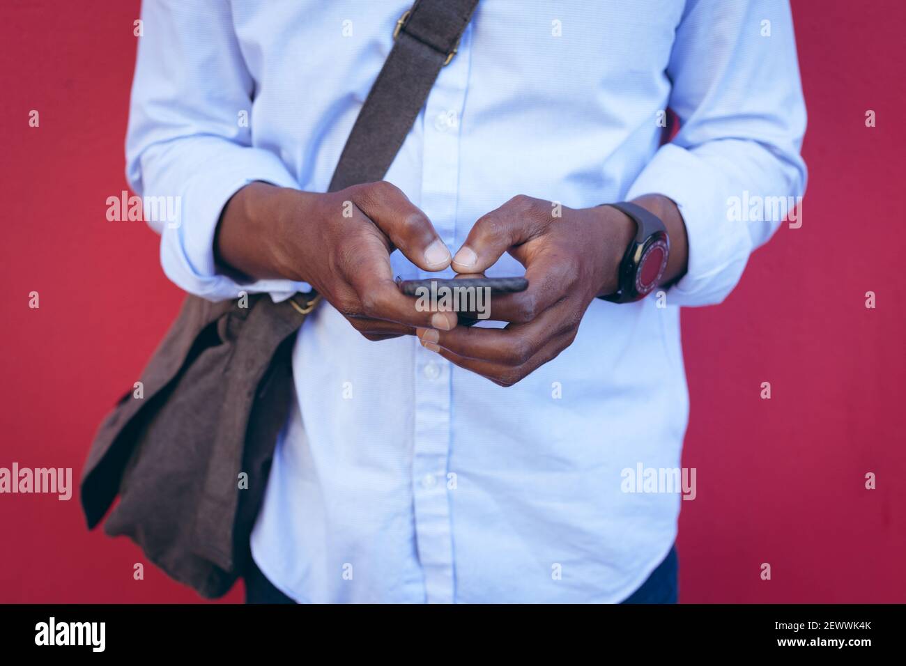 Sezione centrale dell'uomo afroamericano in piedi contro il muro rosso dentro la strada utilizzando lo smartphone Foto Stock