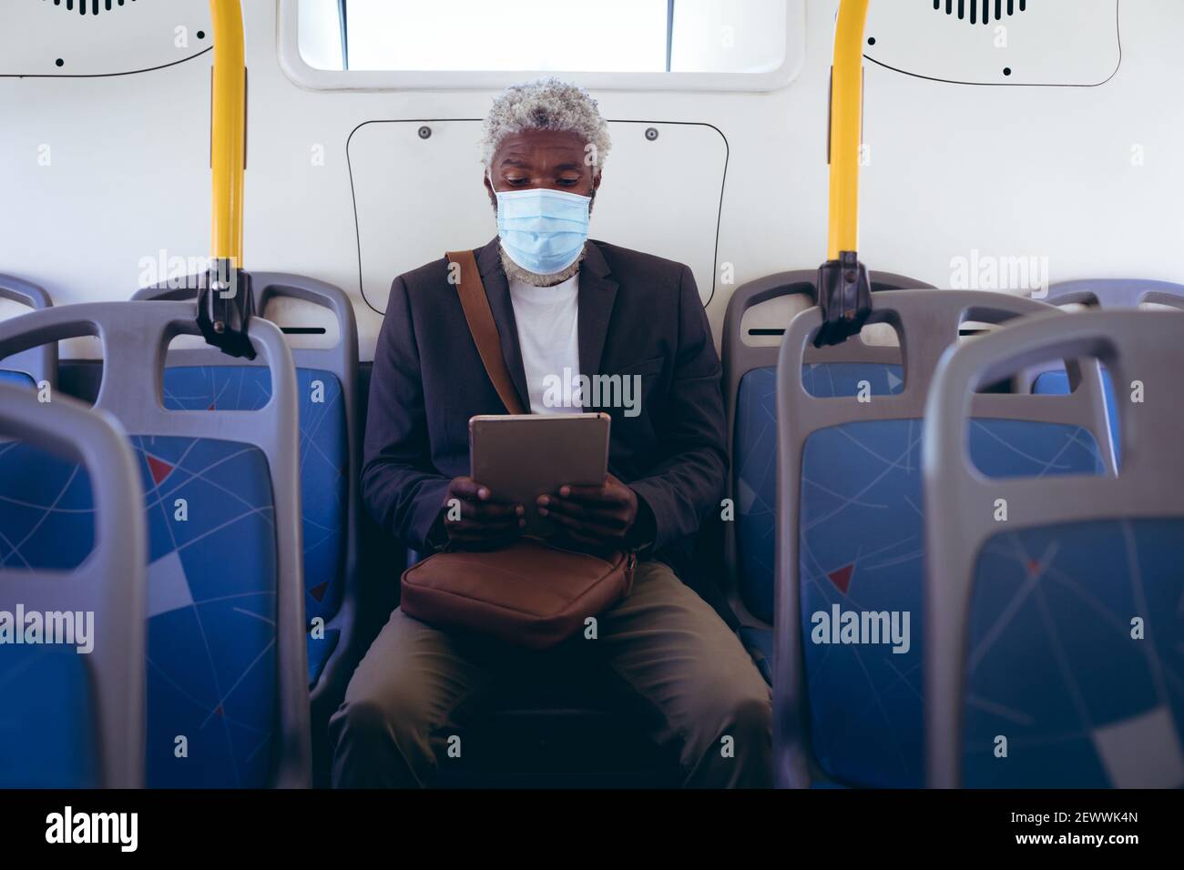 Uomo anziano afro-americano che indossa la maschera di faccia seduto sull'autobus utilizzando un tablet digitale Foto Stock