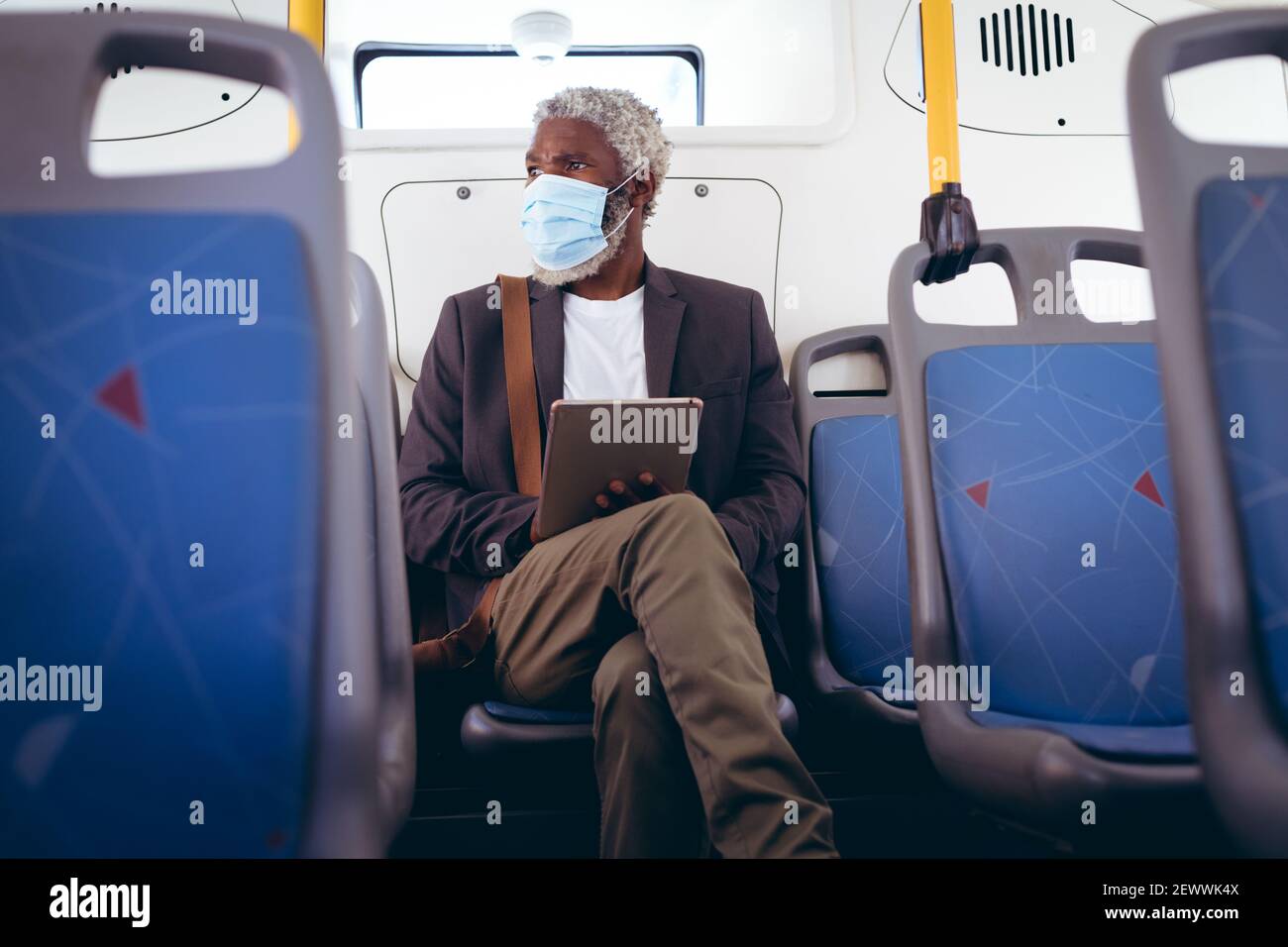 Uomo anziano afro-americano che indossa la maschera di faccia seduto sull'autobus utilizzando un tablet digitale Foto Stock