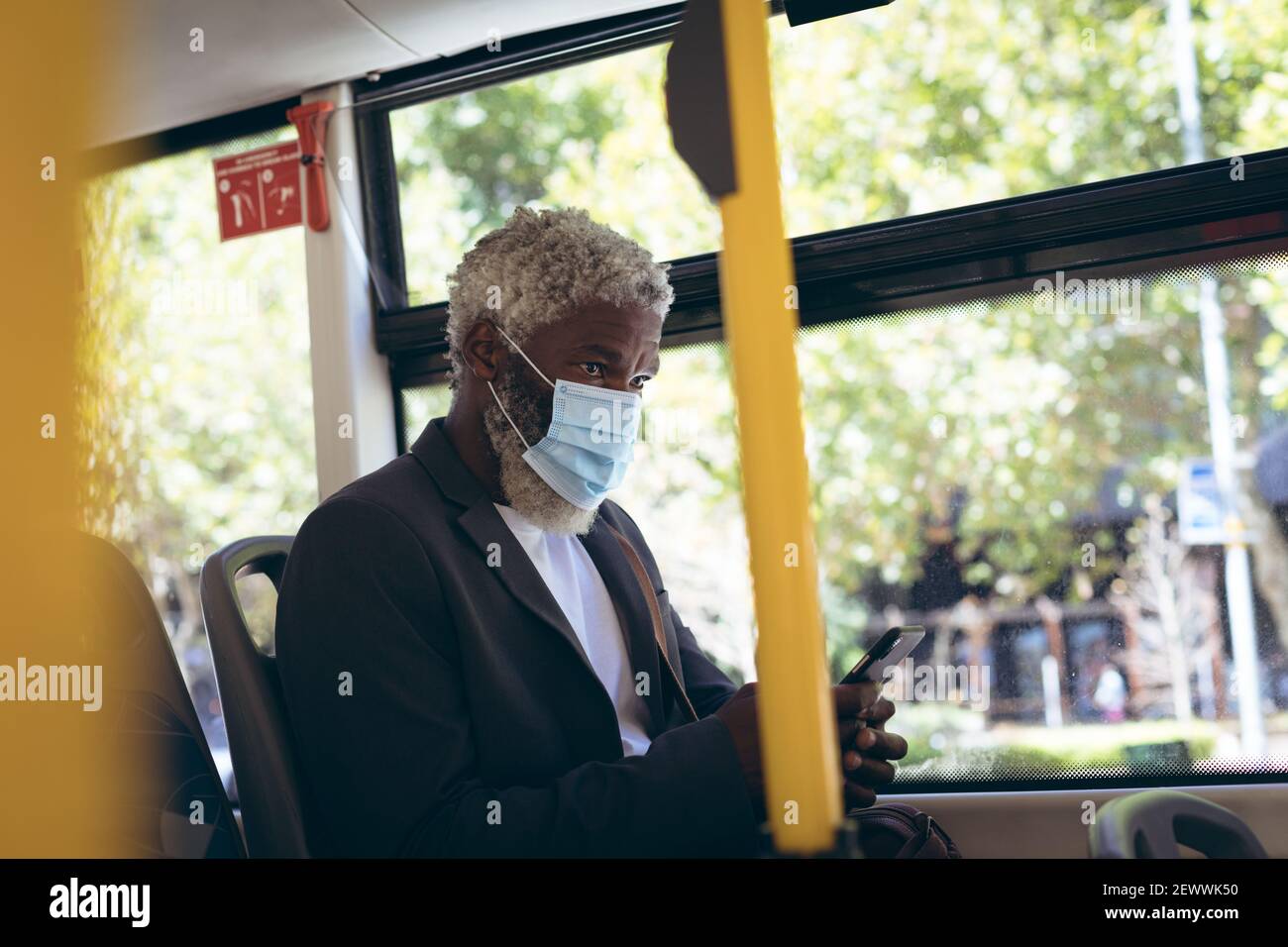 Uomo anziano afro-americano che indossa la maschera di faccia seduto sull'autobus tramite smartphone Foto Stock