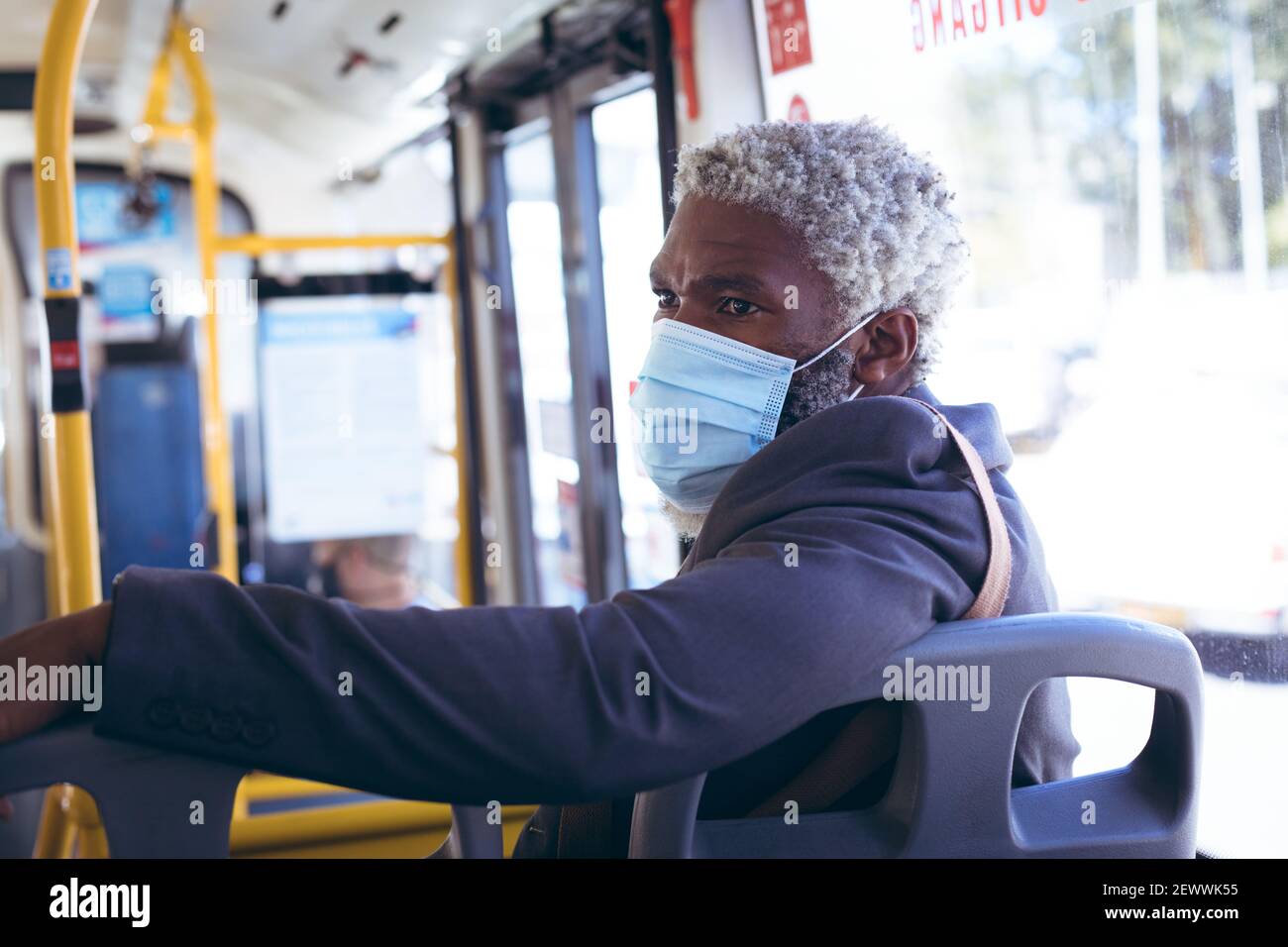 Uomo anziano afro-americano che indossa la maschera di faccia seduto sull'autobus girandosi per guardare Foto Stock
