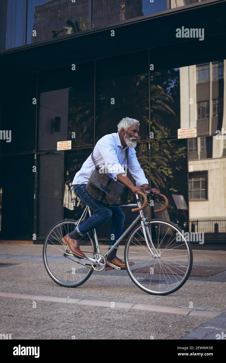 Uomo anziano afroamericano che corre in bicicletta nella strada passato porta Foto Stock