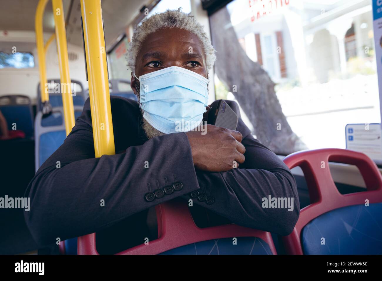 Uomo anziano afro-americano che indossa la maschera di faccia seduto sull'autobus tenere lo smartphone Foto Stock