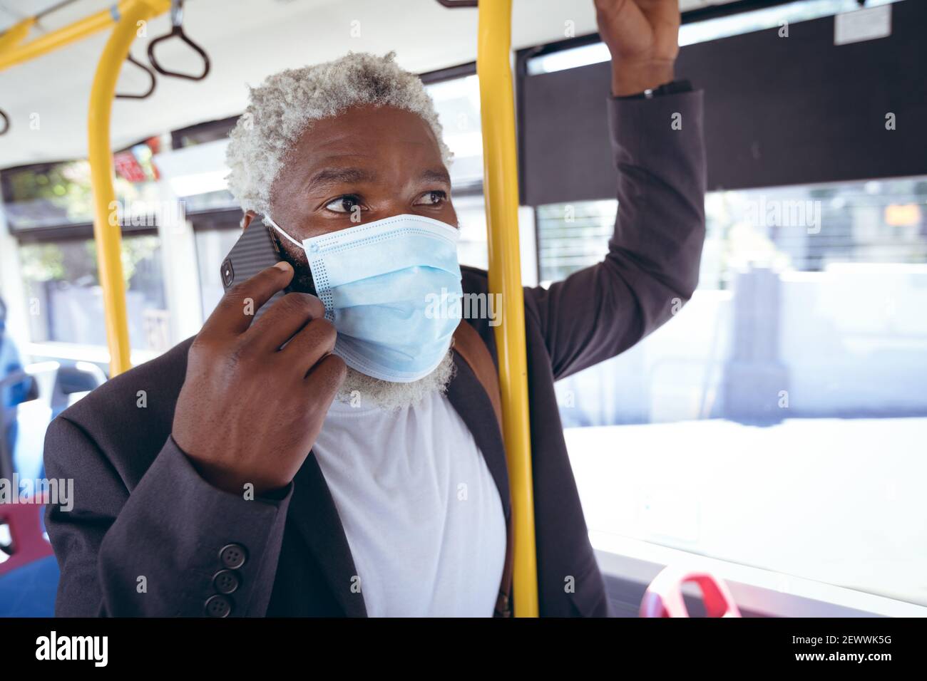 Uomo anziano afro-americano che indossa una maschera facciale in piedi sull'autobus parlare con lo smartphone Foto Stock