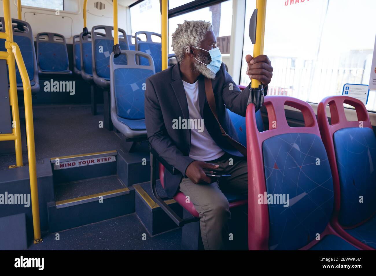 Uomo anziano afro-americano che indossa la maschera di faccia seduto sull'autobus tenere lo smartphone Foto Stock