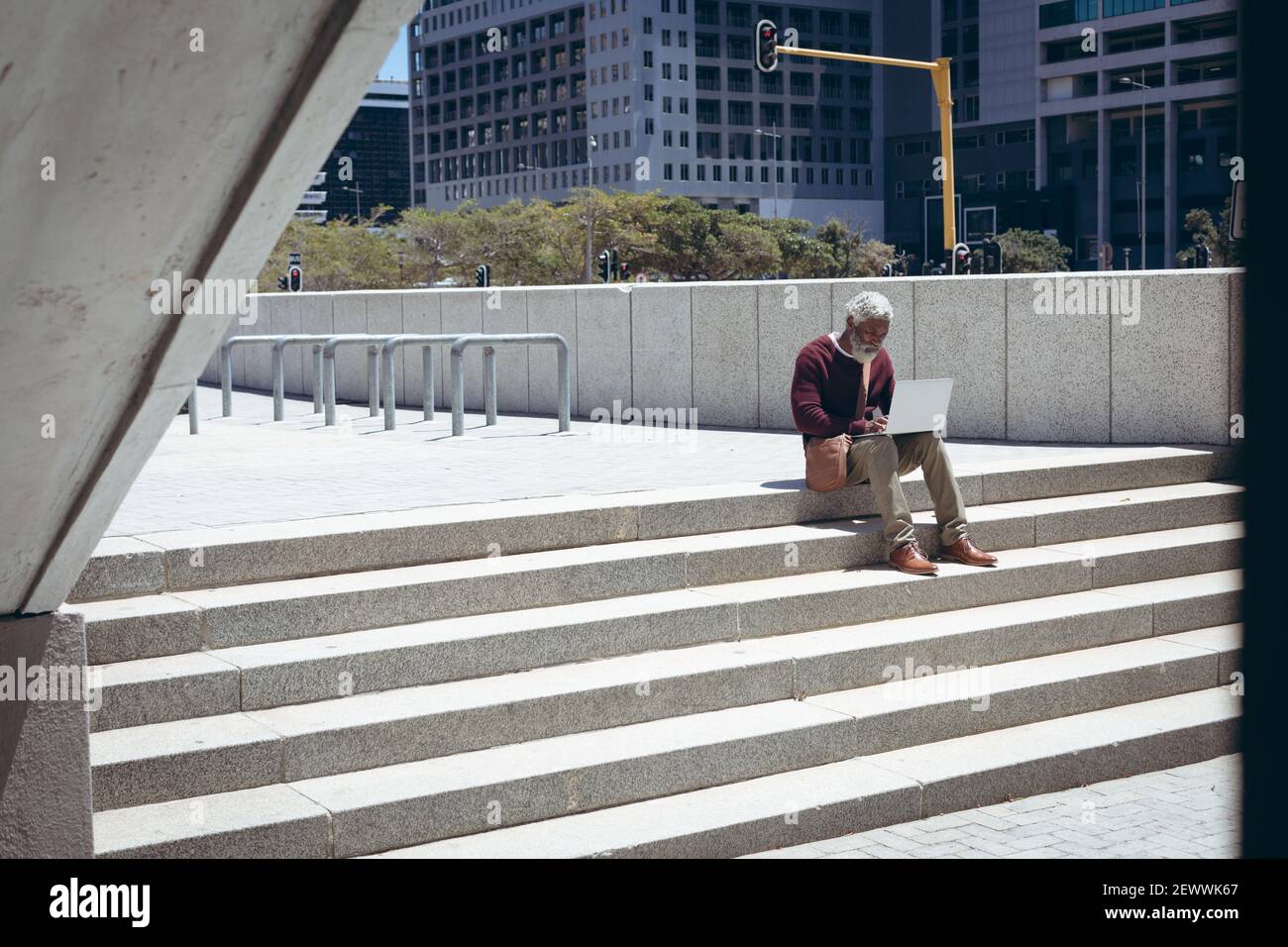 Uomo anziano afroamericano seduto sui gradini della strada utilizzando un computer portatile Foto Stock
