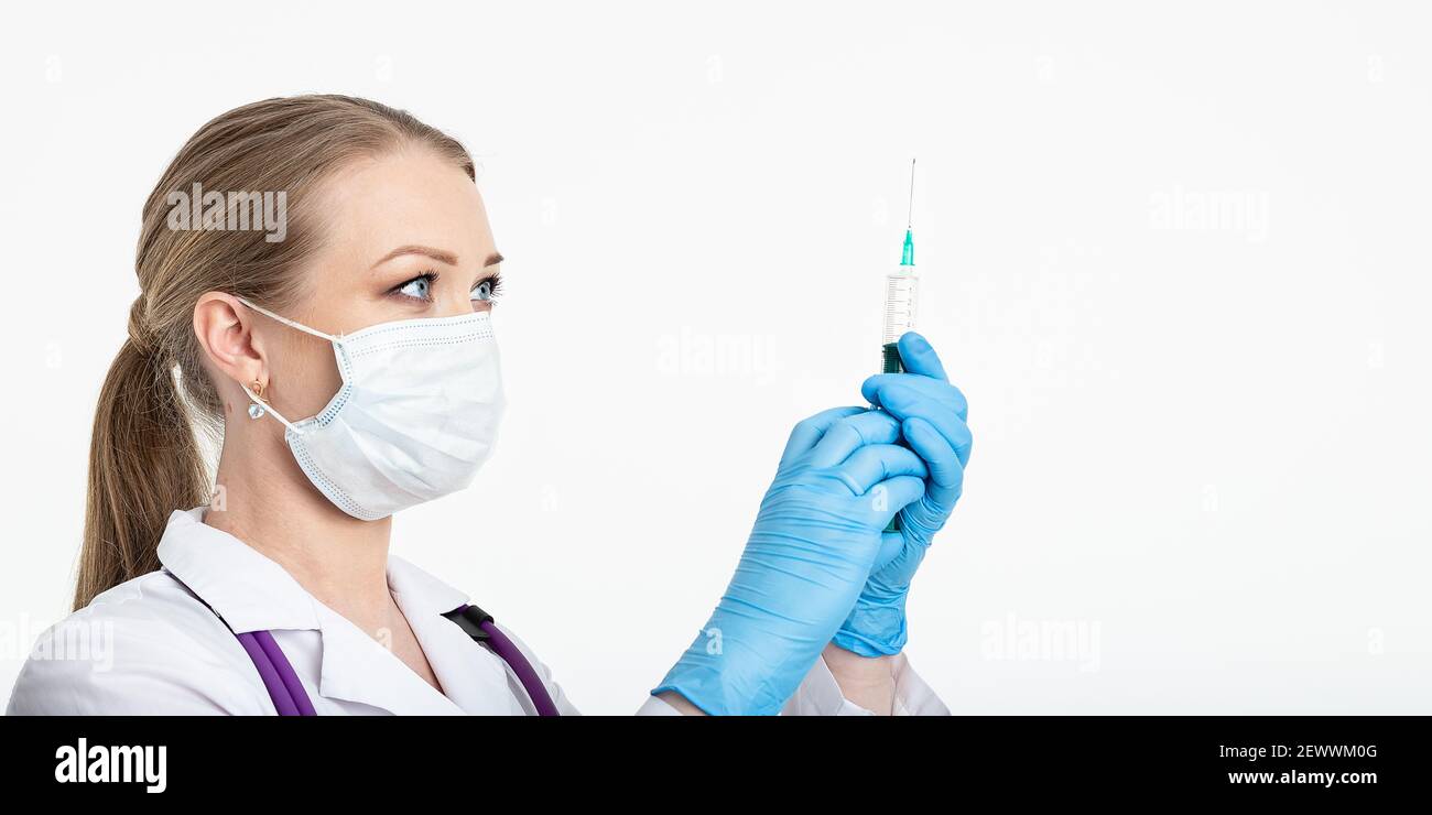 Un giovane infermiere in una maschera compone il vaccino in una siringa mentre si trova in un ospedale accanto a un paziente. Paziente femminile in attesa di iniezione di influenza Foto Stock