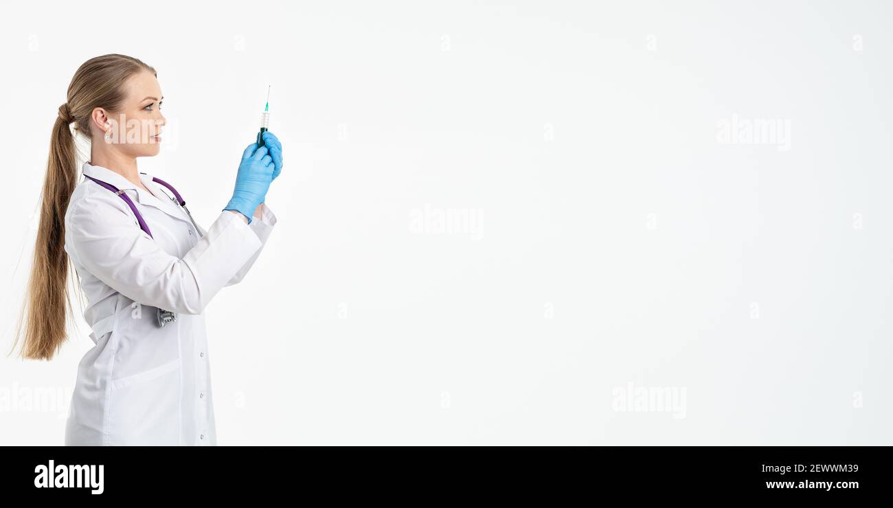 Un giovane infermiere in una maschera e un camice bianco contiene una siringa con un ago per iniezioni, iniezione di influenza, covid. Il concetto di vaccinazione e protezione Foto Stock