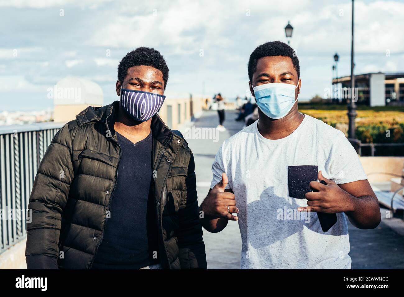 Ritratto di due amici afro-americani con maschera facciale che si posa felicemente su uno spazio urbano. Foto Stock