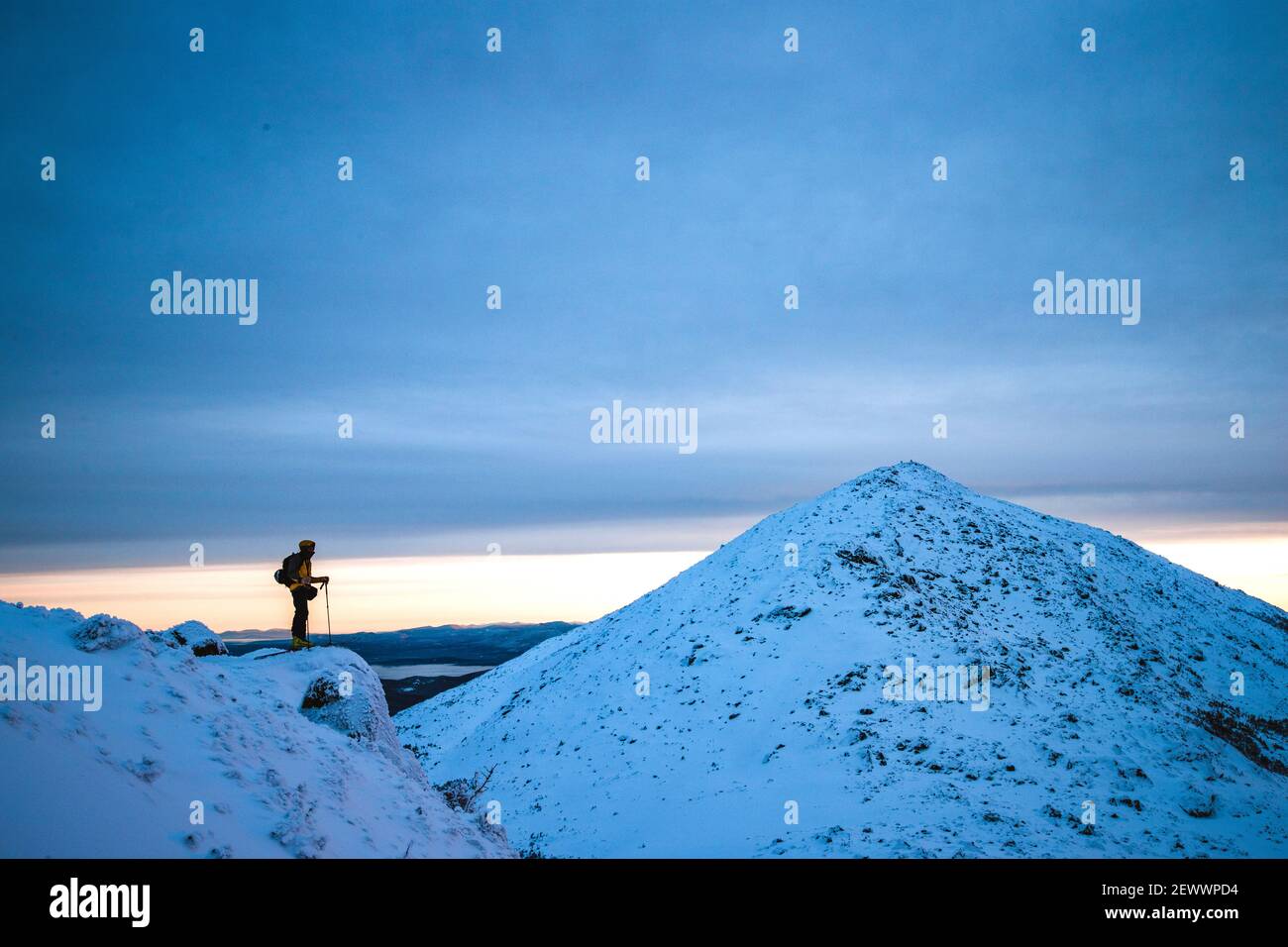 L'uomo si erge sulla scogliera nella neve in inverno guardando montagna distante Foto Stock