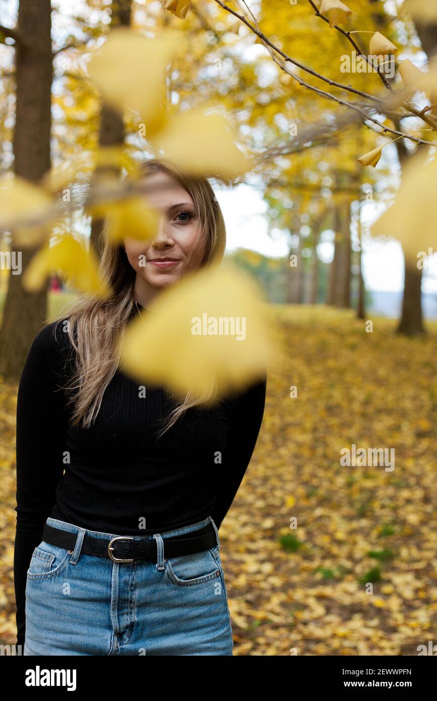 Una giovane bionda si trova sotto un baldacchino di gingko alberi in autunno Foto Stock