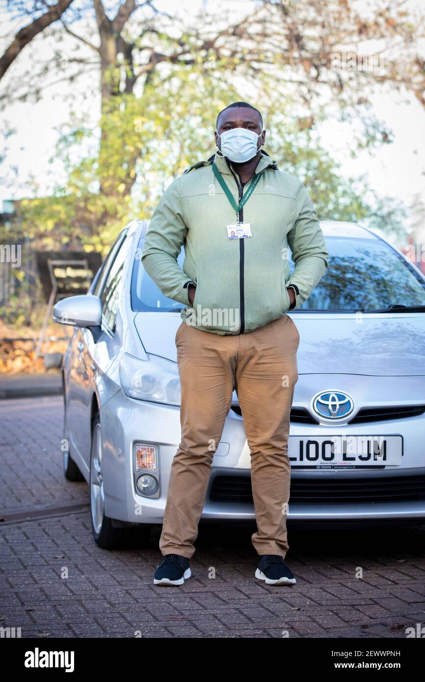 Un conducente privato a noleggio pone con il suo veicolo in un maschera facciale Foto Stock