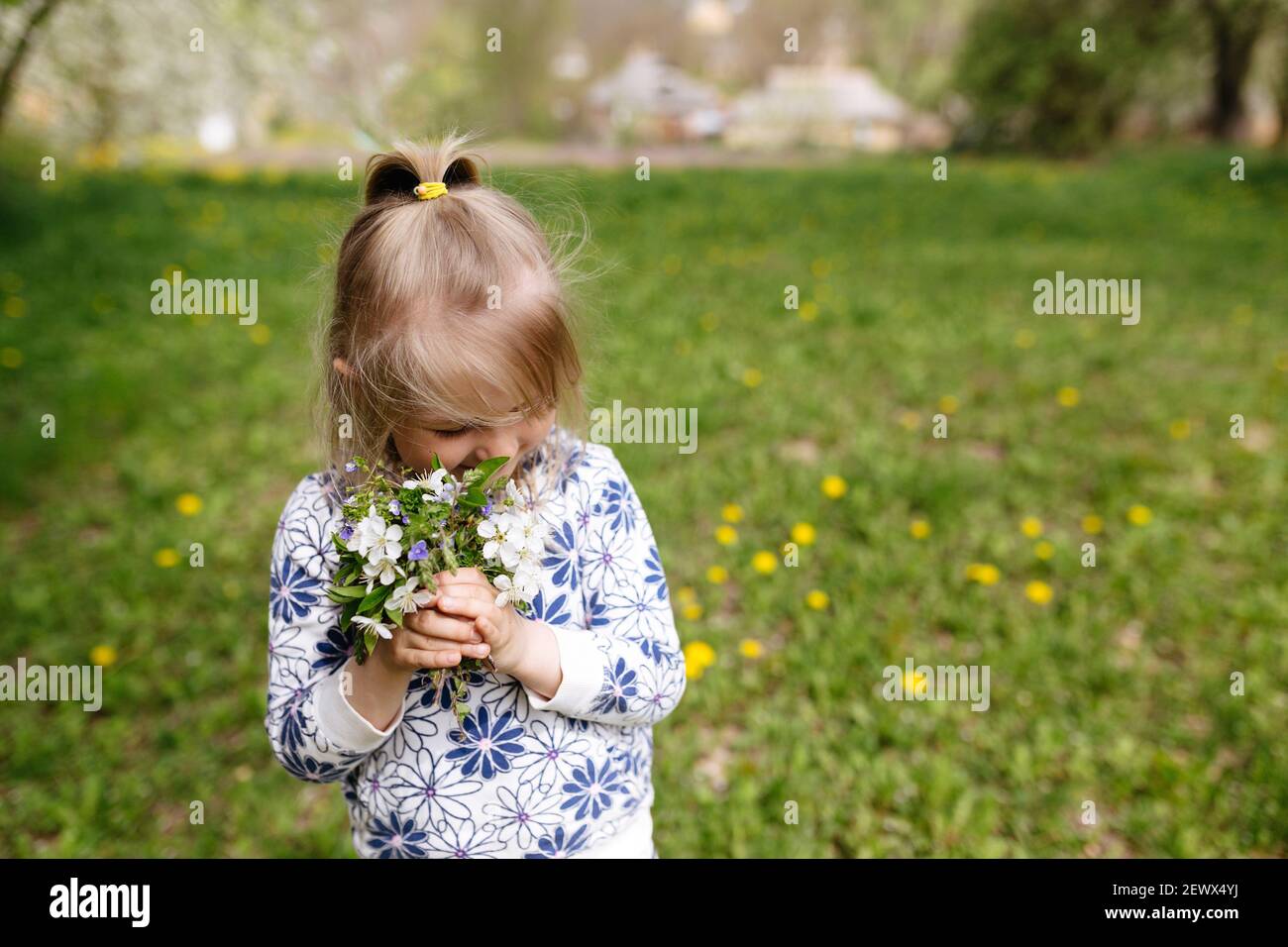 Bambina sniffing fiori primaverili su prato verde in giardino. Foto di alta qualità Foto Stock