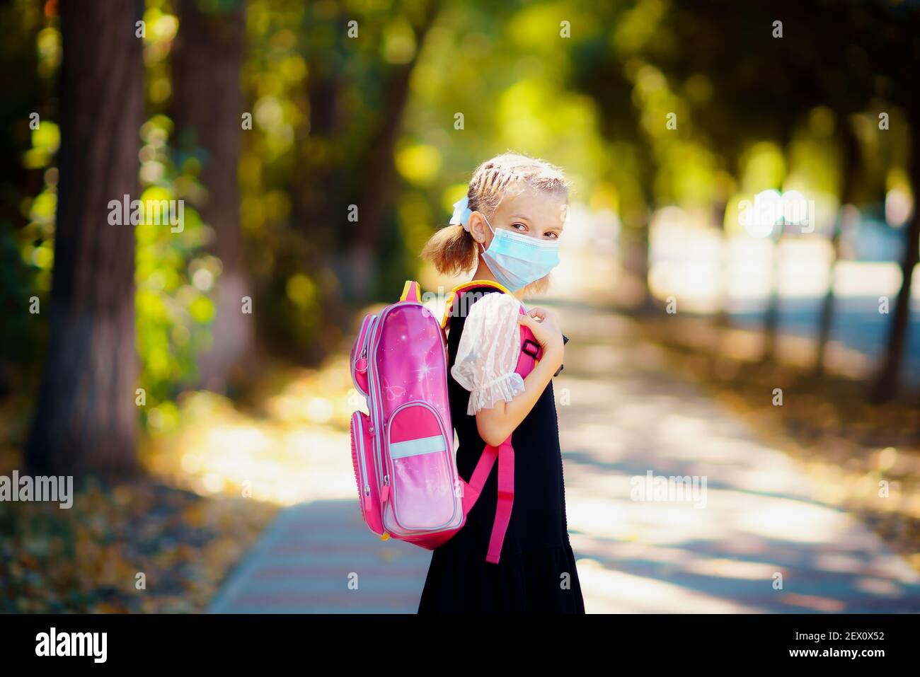 Ragazza della scuola che indossa maschera e zaino per proteggere dal coronavirus. Il bambino va a scuola dopo la pandemia oltre. Foto Stock