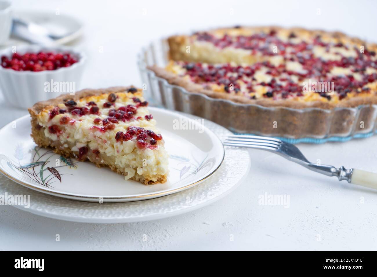 Crostata di cagliata con mirtilli rossi. Aprire la torta rotonda con le bacche su un tavolo bianco. Cottura degli alimenti. Un pezzo di torta su un piatto Foto Stock