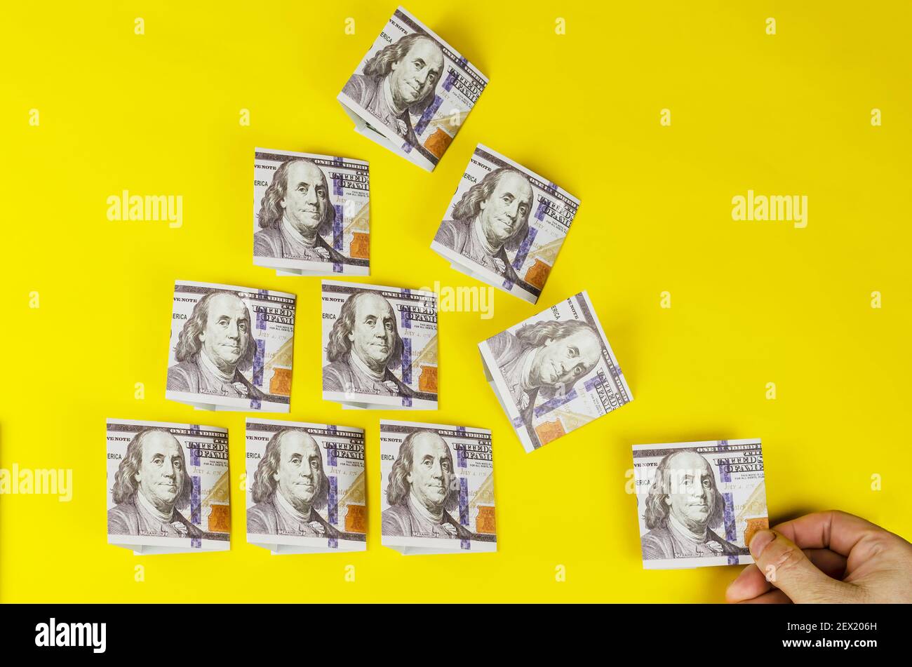 Una mano tira fuori una banconota da dollaro dalla piramide di denaro su uno sfondo giallo. La forma a piramide triangolare di un centinaio di dolla americana Foto Stock