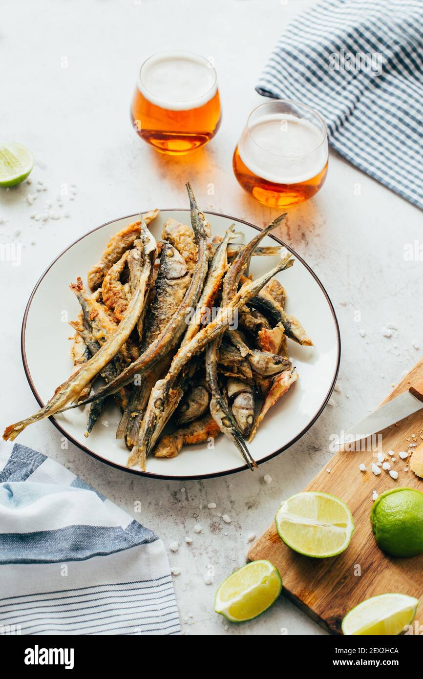 primo piano di acciughe fritte di pesce in un piatto accanto a. birra in bicchieri e lime su un tavolo Foto Stock