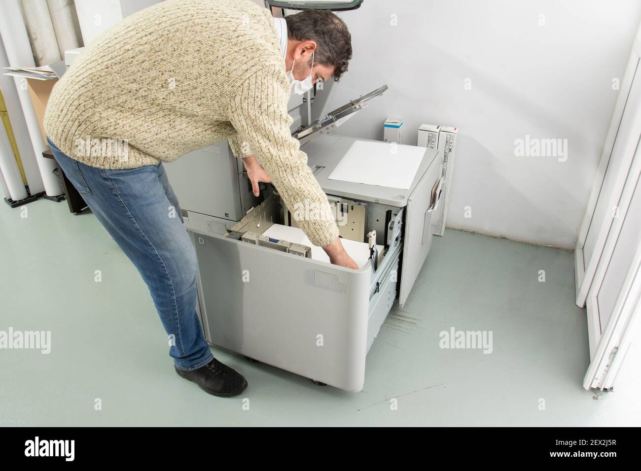 Uomo che lavora in ufficio durante il periodo pandemico con la macchina di stampa digitale. Modi per essere protetti da Covid19. Foto Stock