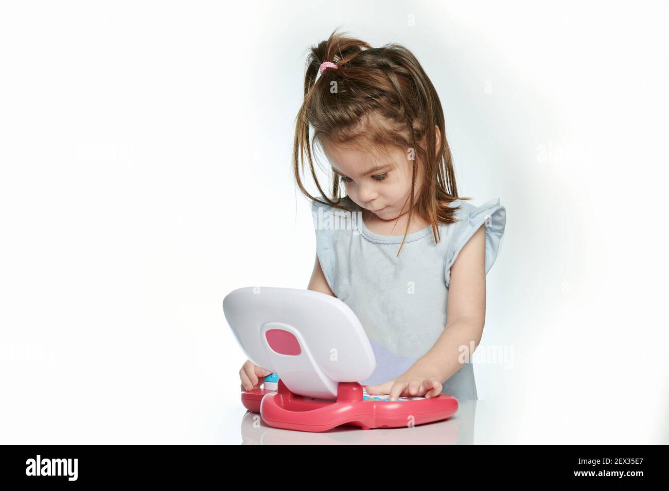 Bambina che usa un computer portatile giocattolo isolato su sfondo bianco dello studio Foto Stock