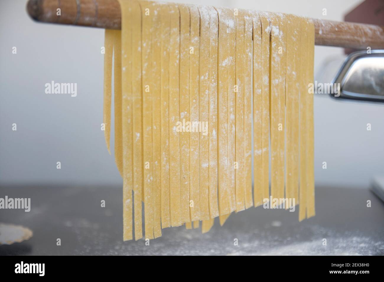 Linguine di pasta fatta in casa appesa su bastone di legno per asciugare.  Tagliatelle italiane fatte in casa appese su un bastone di essiccazione  della pasta Foto stock - Alamy