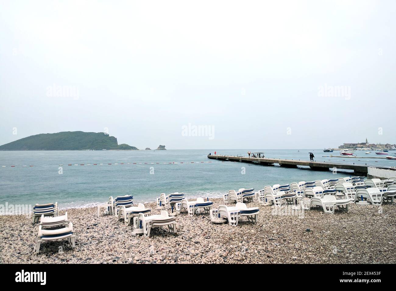 Pioggia autunnale su una spiaggia deserta vicino al Mare Adriatico. Persone sotto gli ombrelloni a bordo della barca. Settembre in Montenegro. Foto Stock