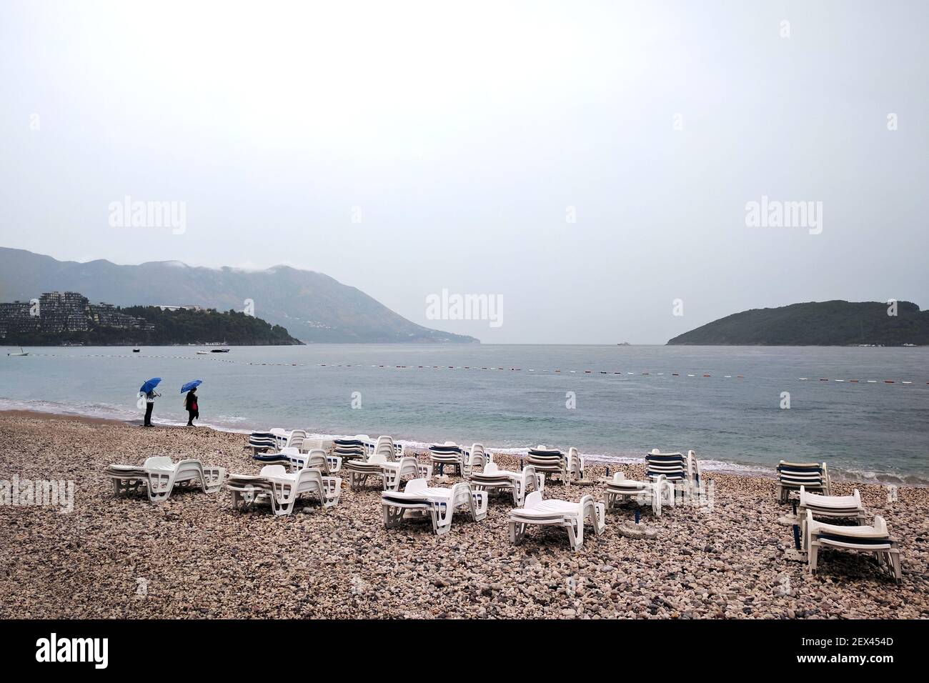Pioggia autunnale su una spiaggia deserta vicino al Mare Adriatico. Persone sotto gli ombrelloni. Settembre in Montenegro. Foto Stock