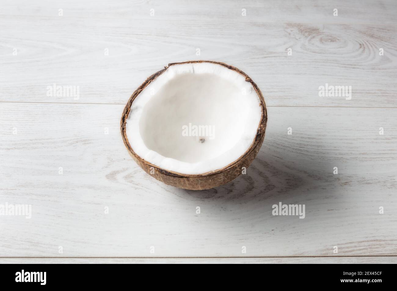 Cocco aperto a metà visto dall'alto con sfondo di legno chiaro. Foto Stock