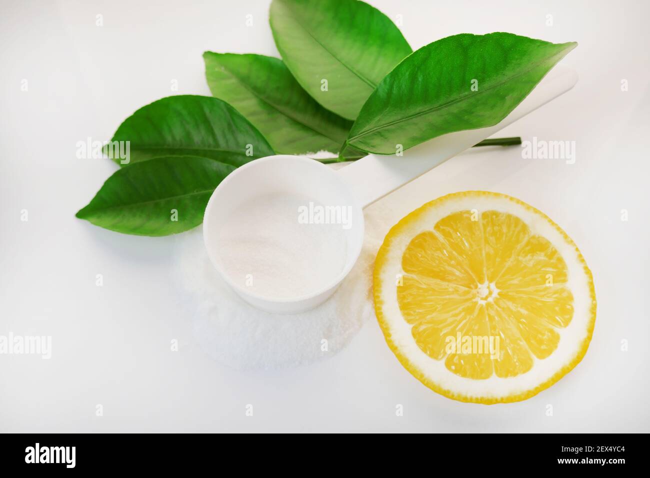 Polvere di vitamina C in un misurino bianco, taglio limone e foglie verdi su uno sfondo bianco.prevenzione di raffreddori e influenza. Un farmaco per il rafforzamento Foto Stock