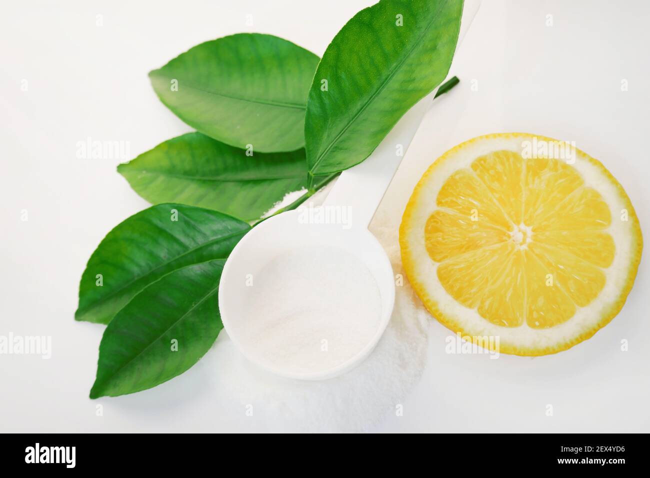 Polvere di vitamina C in un misurino bianco, taglio limone e foglie verdi su uno sfondo bianco.prevenzione di raffreddori e influenza. Un farmaco per il rafforzamento Foto Stock