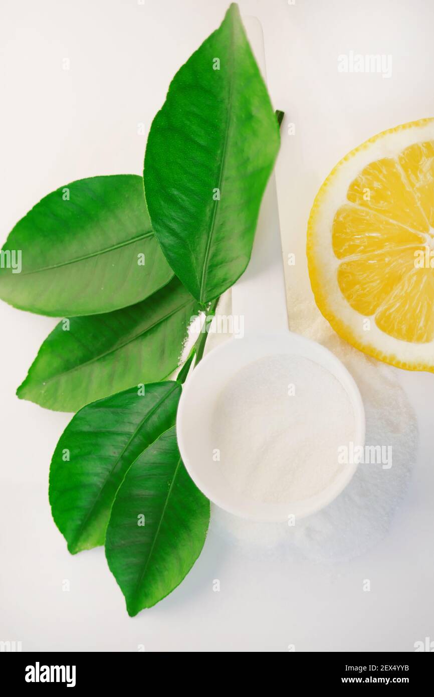 Polvere di vitamina C in un misurino bianco, taglio limone e foglie verdi su uno sfondo bianco.prevenzione di raffreddori e influenza. Un farmaco per il rafforzamento Foto Stock