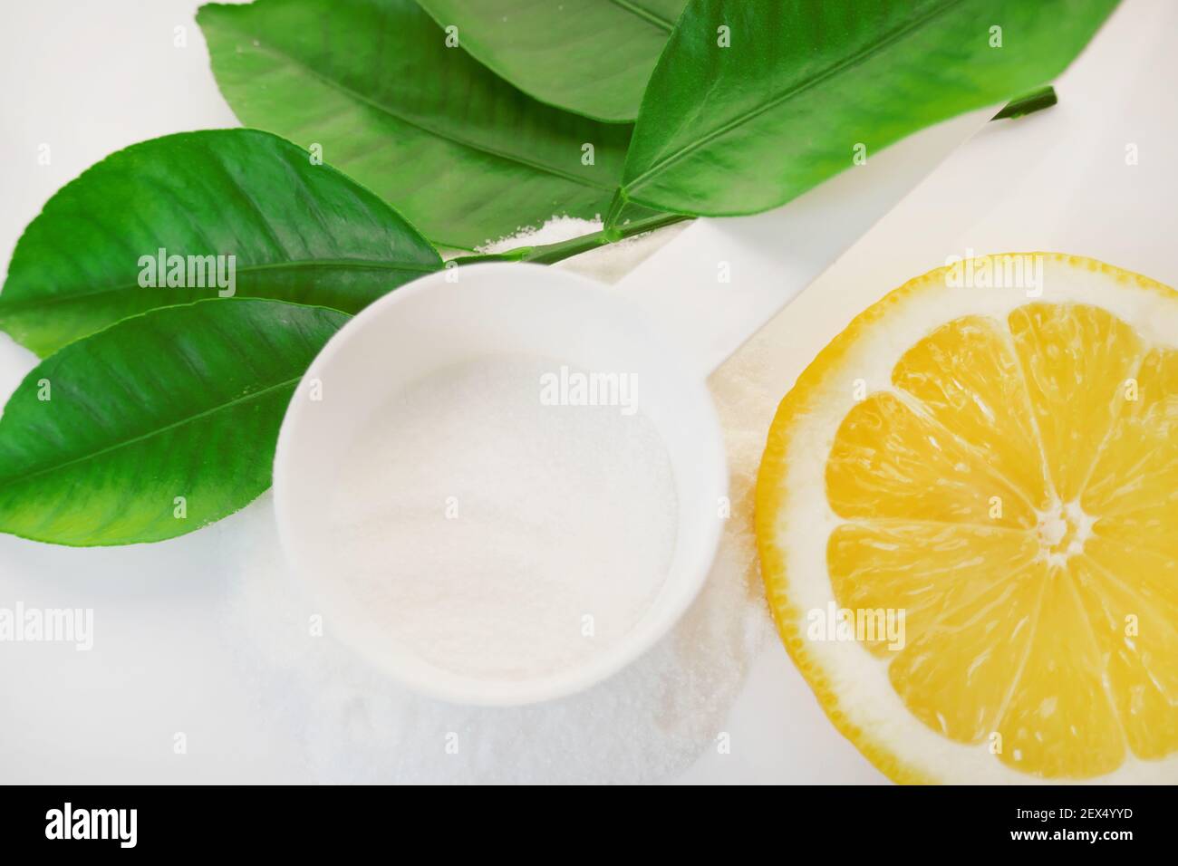 Polvere di vitamina C in un cucchiaio bianco, taglio limone e foglie verdi su uno sfondo bianco.prevenzione di raffreddori e influenza. Un farmaco per rafforzare l'immunità Foto Stock