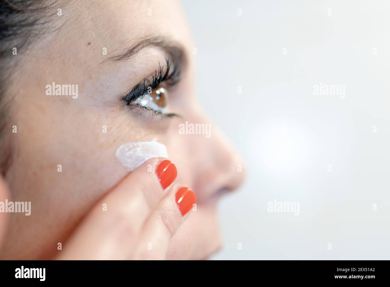 giovane donna che applica crema facciale sul suo viso con le dita nella sua routine quotidiana. cura e concetto di bellezza Foto Stock