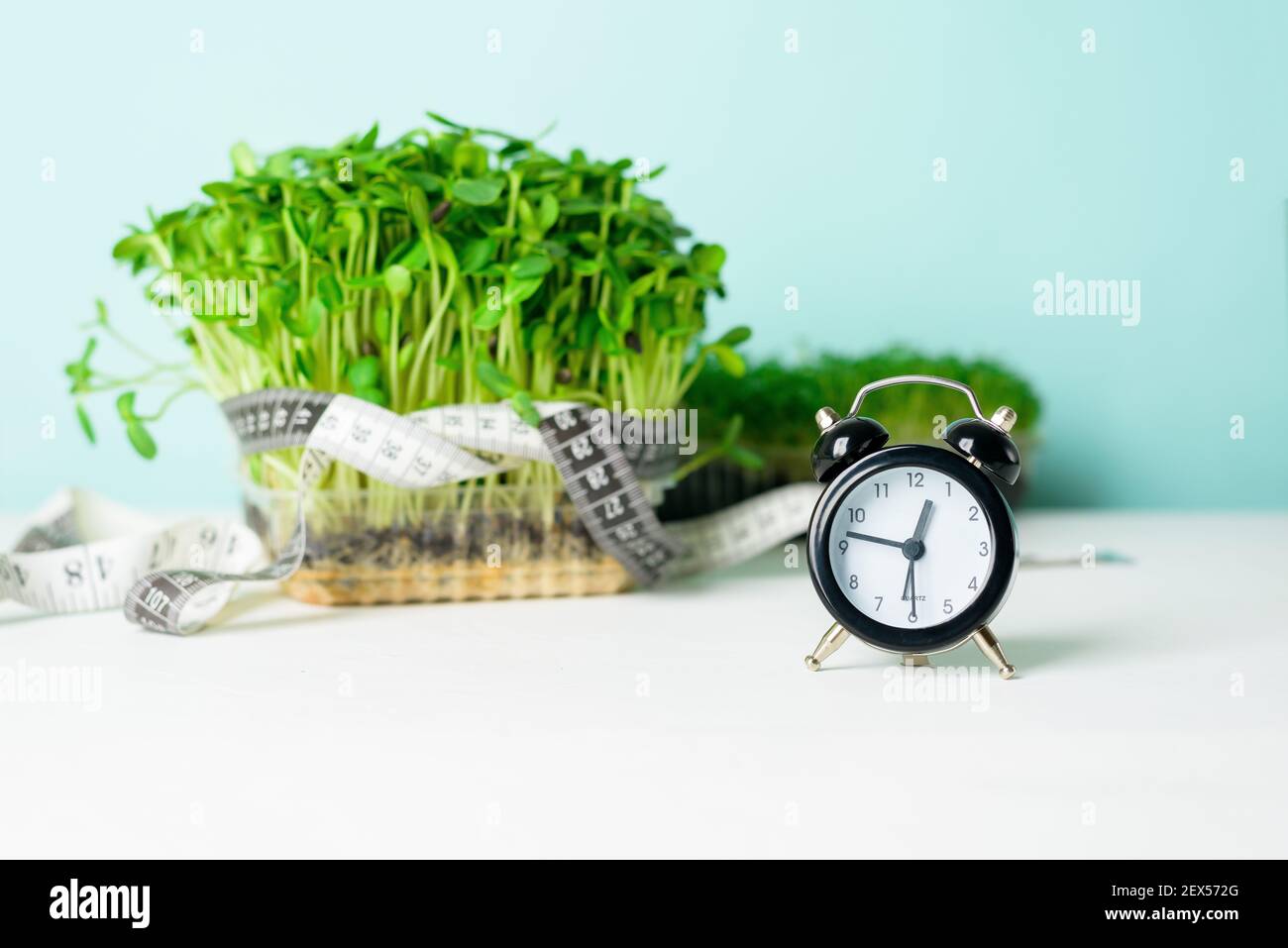 micro-verde sulla scala per la misurazione del peso corporeo, nastro centimetrico per il corpo, orologio su sfondo chiaro. mezzi e oggetti per una dieta, un l sano Foto Stock