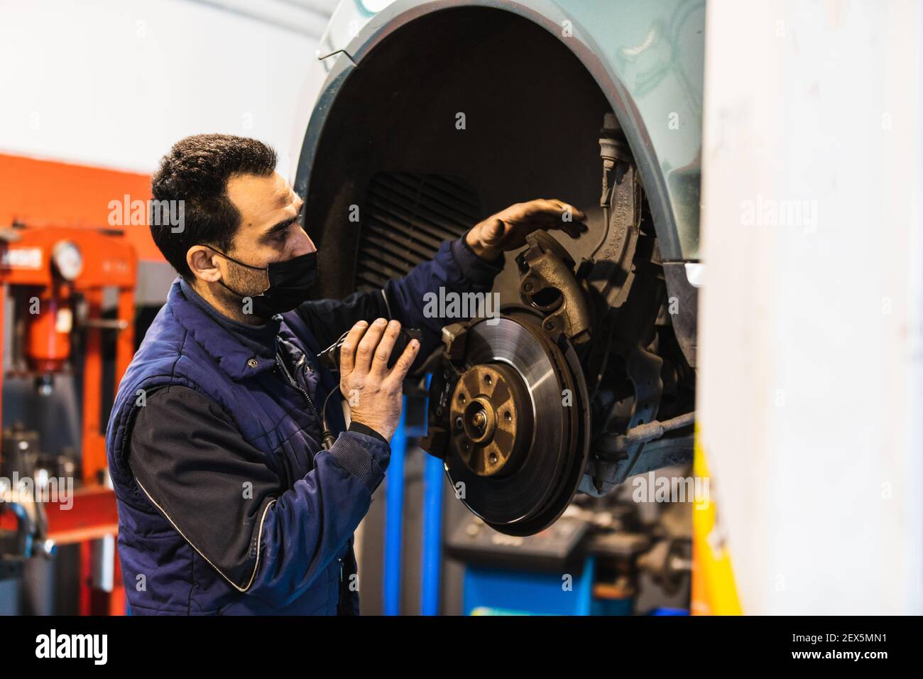 Meccanico che ripara i freni sulla vettura. Maschera. Concetto di riparazione del veicolo con freno a disco di messa a fuoco selettiva Foto Stock