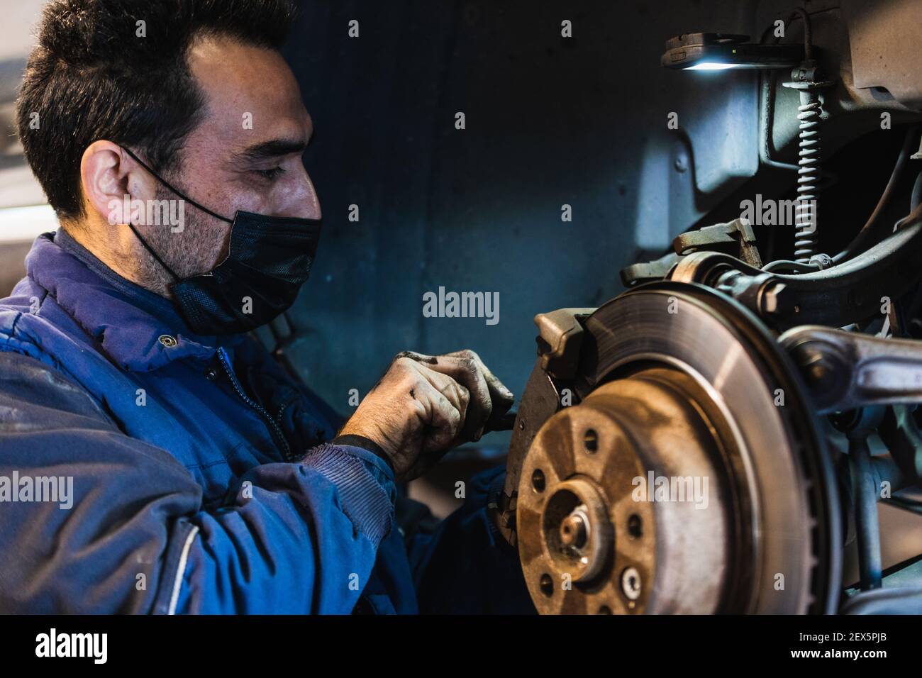 Meccanico che ripara i freni sulla vettura. Maschera. Concetto di riparazione del veicolo con freno a disco di messa a fuoco selettiva Foto Stock